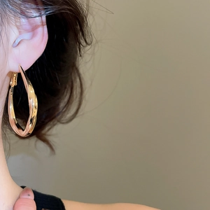 Close-up of golden twisted drop hoop earring on model with elegant metallic luster
