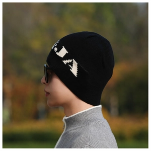 Close-up of black knitted beanie with white jacquard letter branding on a male model