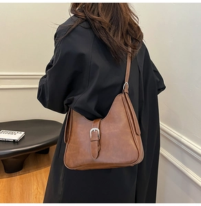 Sac hobo vintage marron caramel porté sur un manteau noir avec une boucle argentée chic