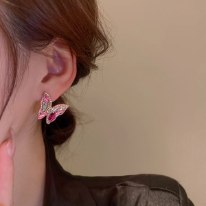 Macro shot of a butterfly stud earring with pink gemstones and gold metal finish