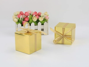 Detail of square gold candy boxes with shiny mirror finish and matching silk ribbons