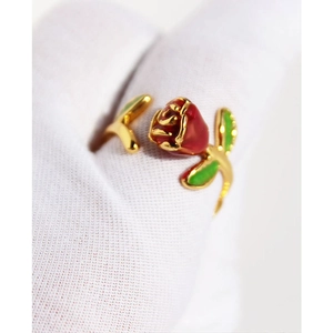 Adjustable gold rose ring with red enamel flower and green leaves on a white glove