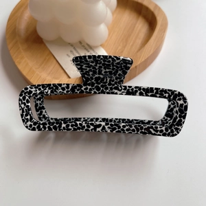 Macro detail of large black and white spotted acetate hair claw clip on white surface