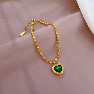 Macro detail of green heart pendant on golden beaded stainless steel bracelet