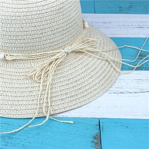 Detail of beige straw sun hat with woven bow tie and small white beads on wooden background