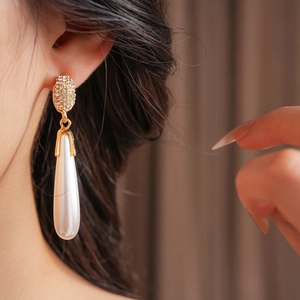 Close-up of gold diamond-set stud earrings with elegant white teardrop pearl pendants