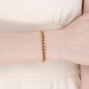 Close-up of a gold Cuban link steel bracelet on a wrist with a soft cream background