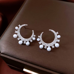 Macro shot of silver C-shaped earrings with sparkling cubic zirconia and white pearls