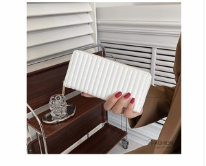 Detail of a beige long wallet featuring vertical quilted patterns and a golden zipper