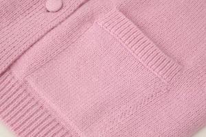 Detail of pink knitted cardigan featuring ribbed hem, button, and textured pocket design