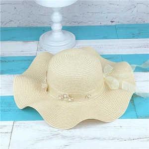 Detailed view of beige straw hat with wavy brim featuring pearl and ribbon flower accents