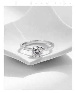 Macro detail of silver ring with round moissanite in classic prong setting on white pedestal