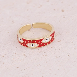 Macro shot of gold-plated evil eye ring with red enamel details on stone texture