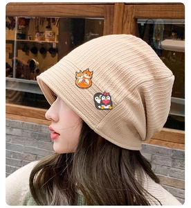 Close-up of beige knitted beanie featuring cute fox and penguin animal cartoon badges