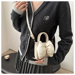 Detailed view of cream bow shoulder bag with top handle and adjustable strap worn by model