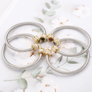 Close-up of four twisted silver steel bracelets with colorful gemstones and gold accents