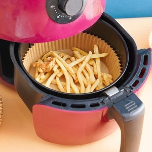 Round brown air fryer parchment paper liners with fried food in a pink fryer basket