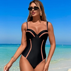 Detail of black one-piece swimsuit with contrast pink trim and high-cut leg on beach