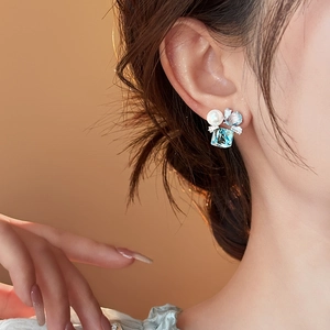Dettaglio ravvicinato dell'orecchino con zircone blu e perla indossato sull'orecchio