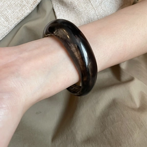 Close-up of a wide acrylic open bangle featuring dark brown marble pattern on model