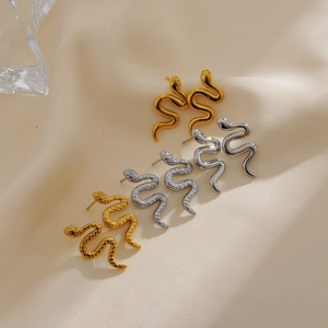 Macro shot of gold and silver snake earrings with scale texture on beige fabric