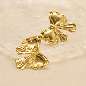 Polished 18K gold bow-knot stud earrings in a decorative textured glass tray
