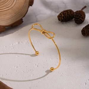 Golden bow knot open bangle displayed on a natural stone base with pine cones decor