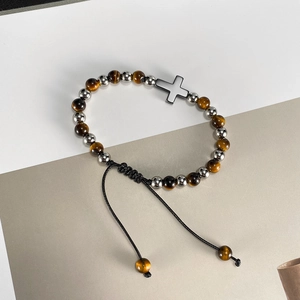 Dettaglio del bracciale con perline occhio di tigre, croce d'argento e chiusura intrecciata