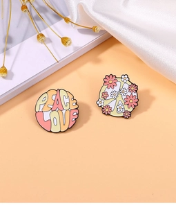 Close-up of Peace Love text and pink flower enamel pin badges on orange backdrop