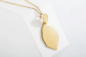 Detailed view of a gold-plated leaf pendant with intricate镂空 vein textures on a white stand