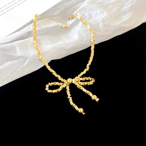 Détail macro du collier nœud doré avec perles métalliques sur fond noir et blanc
