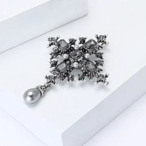 Baroque cross brooch with grey crystals and teardrop pearl pendant on a white platform