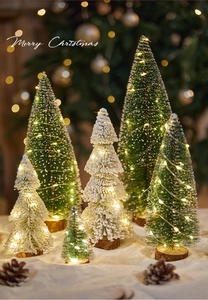 Close-up of mini snowy Christmas trees with warm LED lights on a natural wooden base