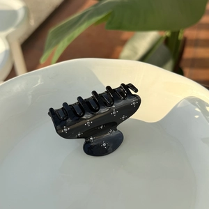 Elegant black acetate hair claw clip with white star-like rhinestones on a white plate