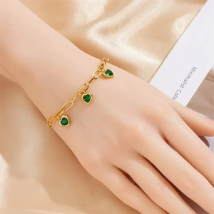 Gold chain bracelet featuring green heart gemstones on elegant champagne silk backdrop