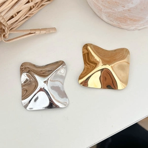 Macro detail of wave-shaped polished metal hoop earrings in gold and silver finish