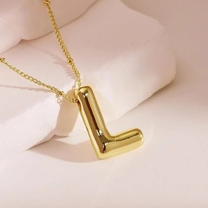 Close-up of golden letter L balloon pendant necklace on a decorative white stone block