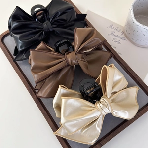 Three oversized faux leather bow hair claws in black, brown, and gold on a wooden tray