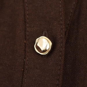 Détail d'un bouton doré irrégulier sur le tissu en lin marron d'une robe chemise sans manches