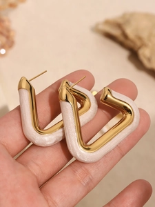 Detailed close-up of golden U-shaped earrings with white pearlescent resin finish
