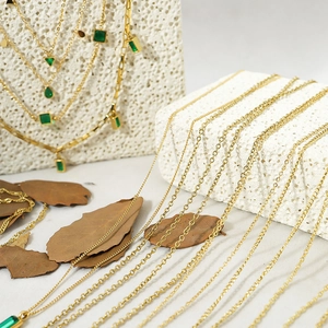 Close-up of gold necklaces with emerald green geometric stone pendants on stone base