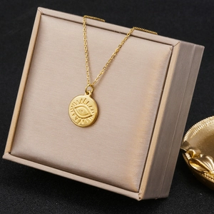 Close-up of gold stainless steel necklace with eye-engraved round pendant on gift box