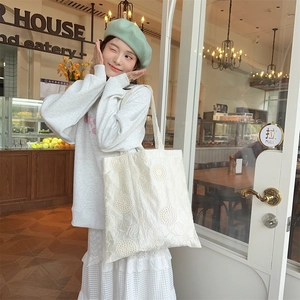 Detailed shot of white hollow lace embroidery on a large canvas tote bag in a cafe