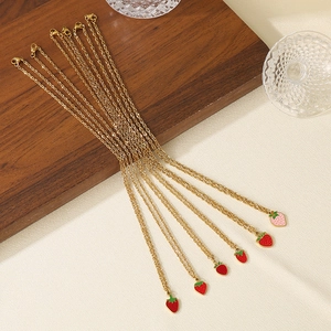 Detail of multiple gold titanium necklaces with red enamel strawberry pendants on fabric