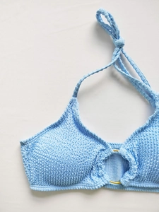 Détail du haut de bikini bleu clair avec tissu froissé et anneau doré central