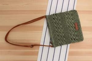 Detail of army green straw woven bag featuring brown leather strap and label on wood