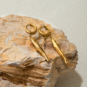 Macro shot of gold fish-shaped hammered stainless steel earrings on a rustic stone base