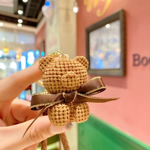 Close-up of brown resin bear keychain with knitted texture and a golden bow detail