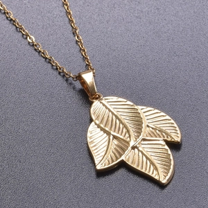 Macro shot of gold stainless steel triple leaf pendant showing detailed texture and shine