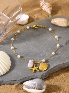Detail of beach-style gold necklace with seashell star pendants and white pearls on rock